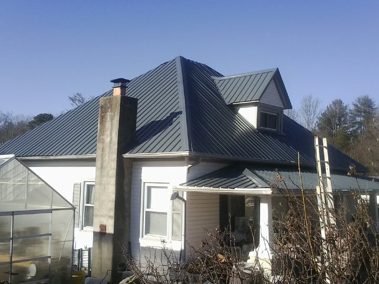 Dark blue standing seam metal roof on a white farmhouse with dormer — Slate & Tile Roof Repair by Roofing Brothers in Alberta