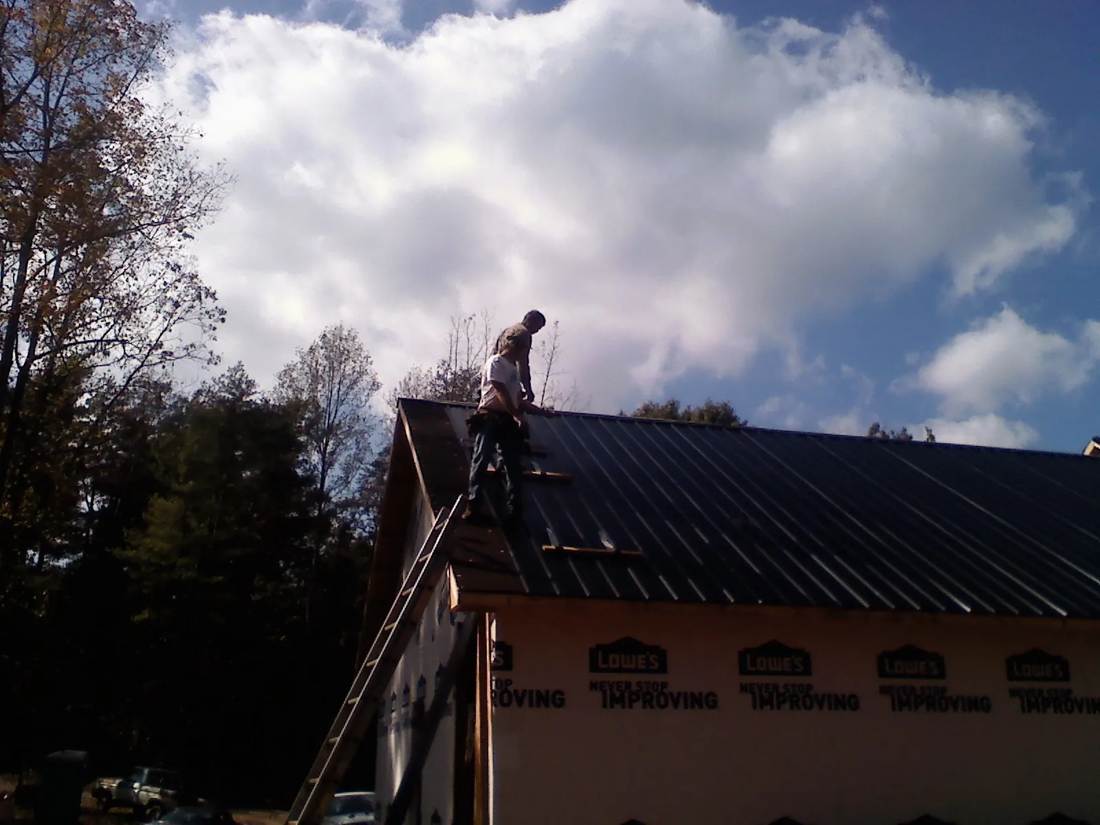 Roofer fastening dark metal panels high against a cloudy sky, from a Roof Inspection job in Alberta